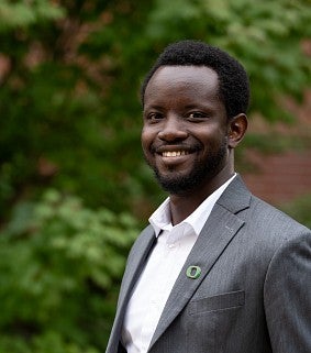 Joel Sati smiles in front of a backdrop of foliage