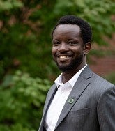 Joel Sati smiles in front of a backdrop of foliage